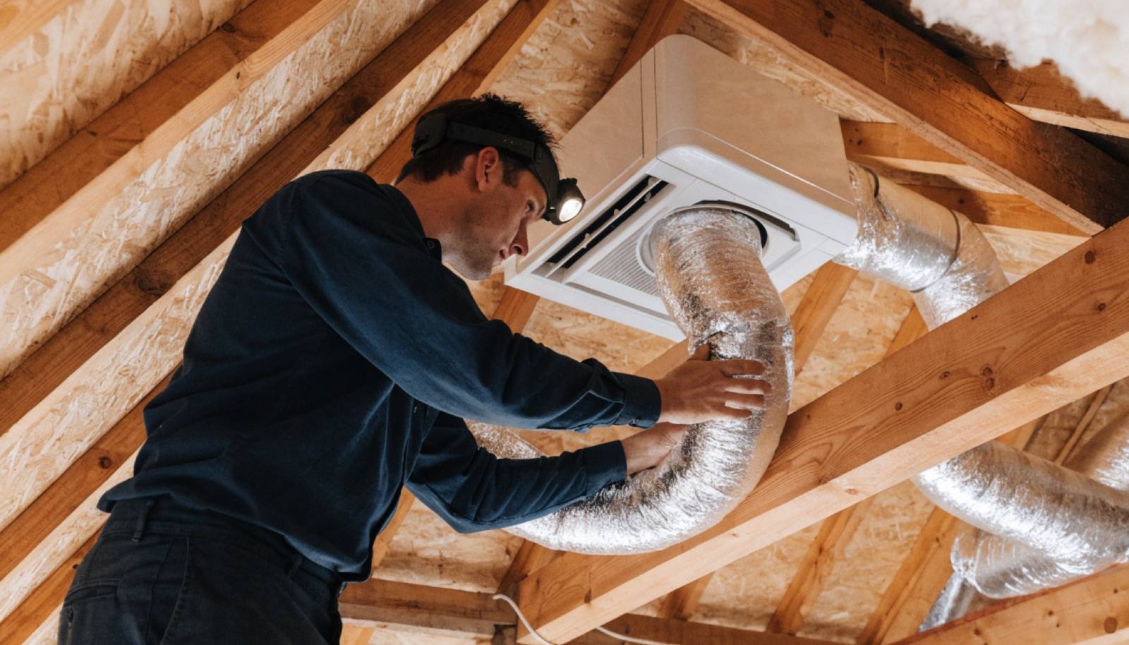 Technician connecting insulated ducting to a ducted air conditioning unit in a roof space