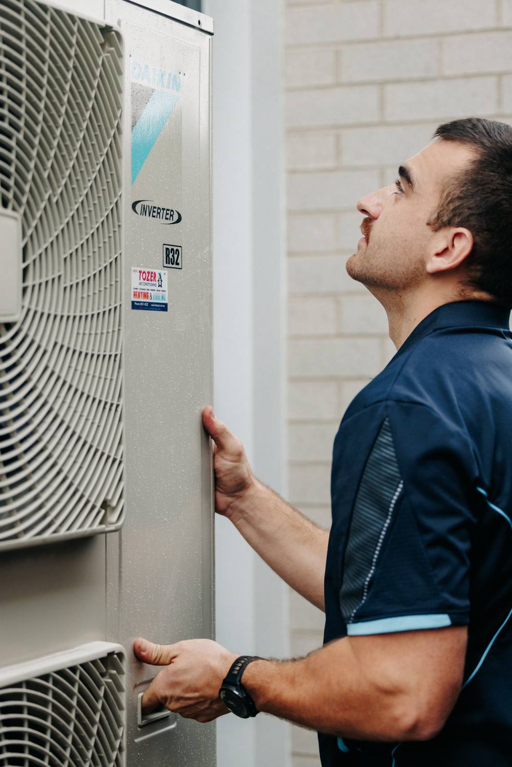A TOZER technician checking a Daikin inverter outdoor unit beside a home