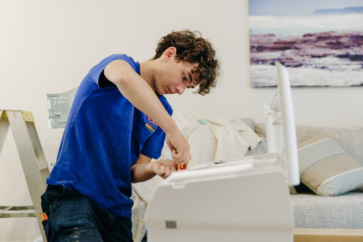 A TOZER technician working on a wall-mounted split system indoor unit in a lounge room
